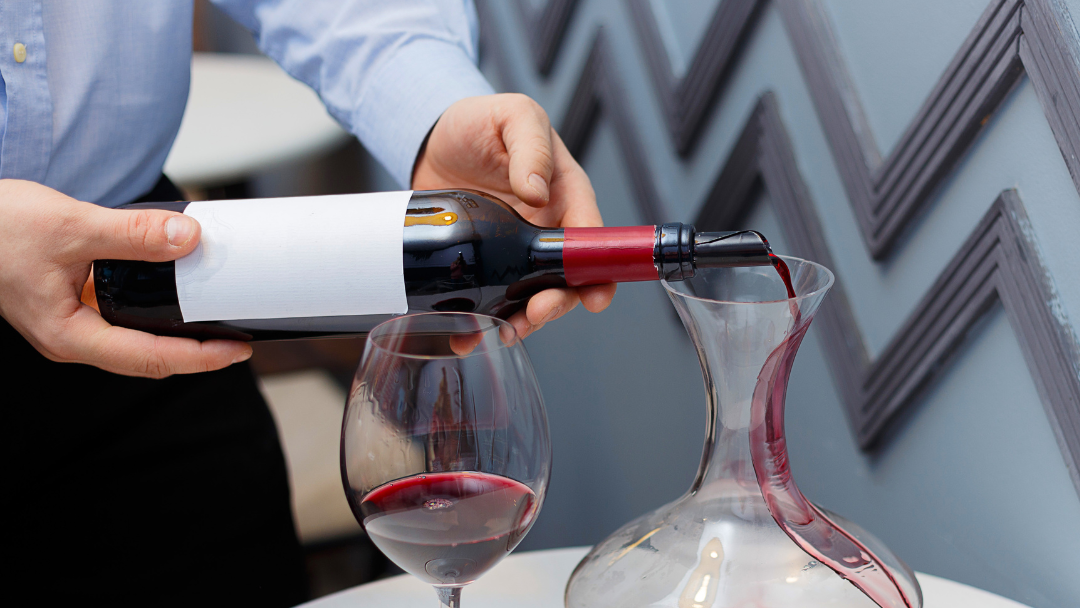 Carafe à décanter en verre avec du vin rouge versé, vue de face sur fond sombre